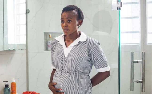 A still fro Netflix show Baby Farm with a woman in a grey and white dress stood in a bathroom